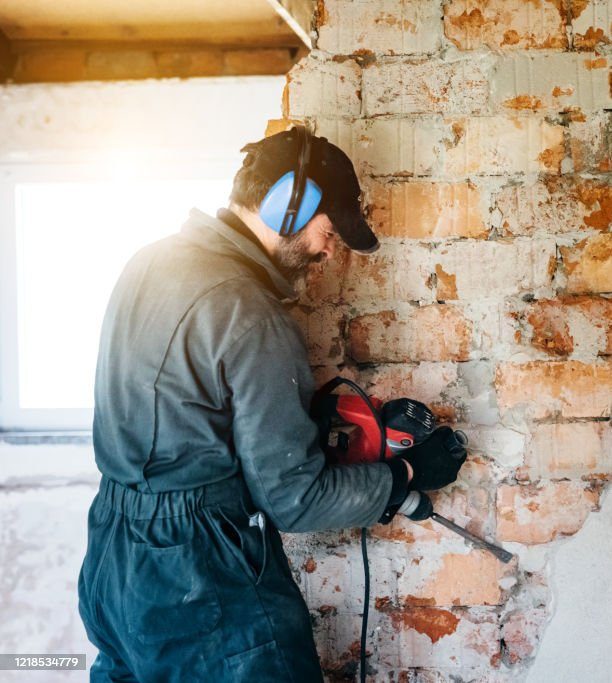 Handwerker mit einer Maschine bearbeitet eine gemauerte Wand.