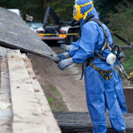 Arbeiter in Schutzanzug hebt eine Asbestplatte auf einer Baustelle.