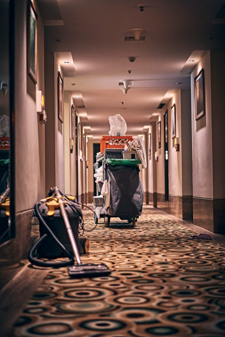 Reinigungswagen und Staubsauger im Flur eines Hotels mit Teppichboden.